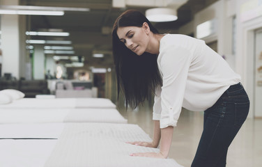 A woman chooses a mattress in a store. She stands next to him and examines him.
