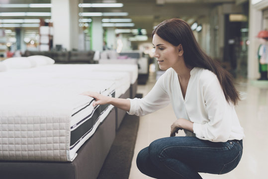 A woman chooses a mattress in a store. She sits next to him and examines him
