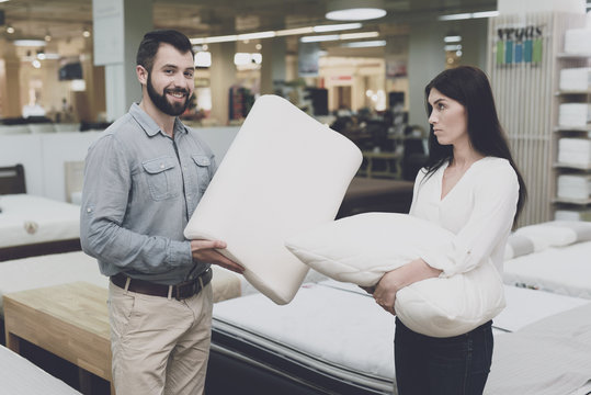 A couple in a large store of beds and mattresses chooses pillows. They examine several variants of pillows