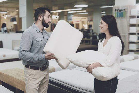 A couple in a large store of beds and mattresses chooses pillows. They examine several variants of pillows