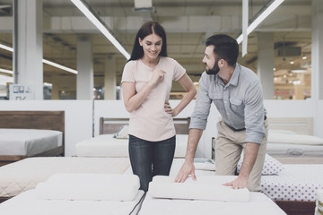 A couple in a large store inspects the mattress before buying. They stand next to him and study him