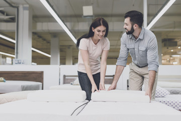 A couple in a large store inspects the mattress before buying. They stand next to him and study him