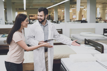 Consultant-orthopedist helps the girl to choose a mattress in the store. He interrogates a woman