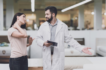 Consultant-orthopedist helps the girl to choose a mattress in the store. He interrogates a woman