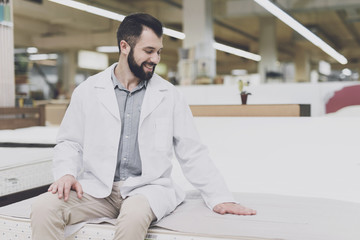 A man in a white robe sits on the edge of the mattress and looks at him. He put his hand on him