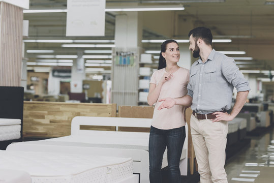 A couple chooses a mattress in the store. A woman points at one of them. A man is standing by