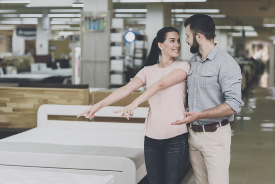 A couple chooses a mattress in the store. A woman points at one of them. A man is standing by