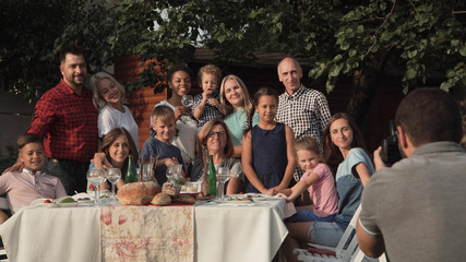Cheerful family standing at table in garden and posing for photo. - obrazy, fototapety, plakaty
