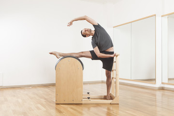 Pilates instructor performing exercise on barrel equipment