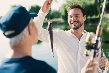 A man with a spinning in his hands brags at the old man, who is ahead of him with the fish he just caught