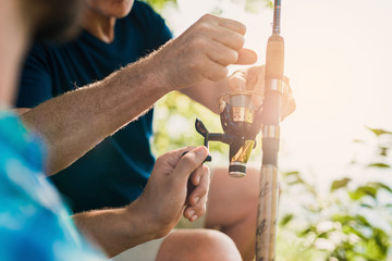 The old man helps the man untangle the line on the spinning reel