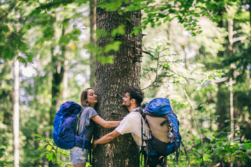 Hiking couple. Young couple with backpacks hugging tree and having fun 