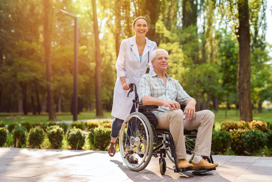 Doctor with old man in wheelchair walking in sunny park