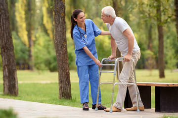 Fototapeta premium A nurse helps a pensioner to walk in the park on adult stilts