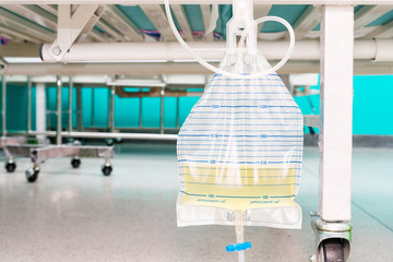 Urine bag hanging beside the patient's bed. Inside the hospital room.