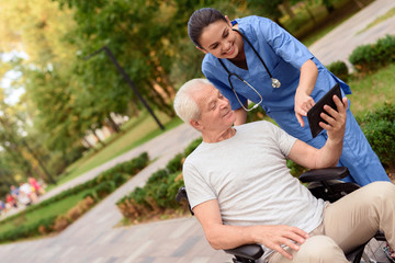 Naklejka premium A nurse and an old man are looking at something on an old man's tablet