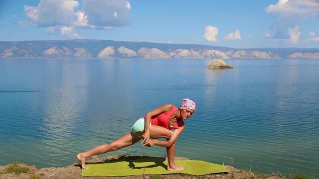 professional yoga woman practices yoga moves outdoors. blue lake baikal on the background