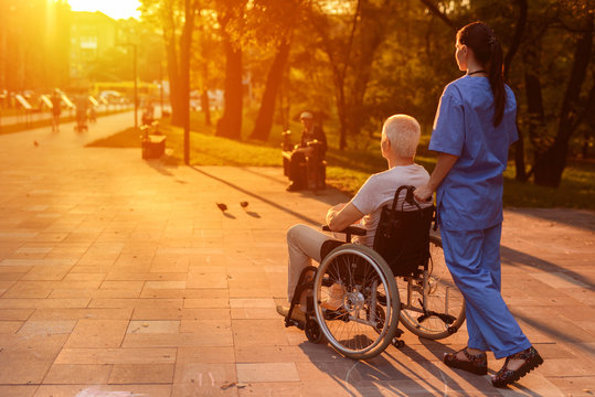 Nurse and old man who sits in a wheelchair watching the beautiful sunset in the park