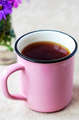 A pink mug of black tea on a light background and purple flowers.