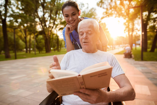 A nurse watches as the old man reads a book in the park at sunset