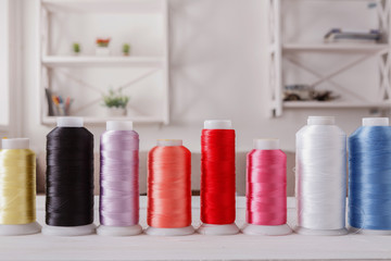 Colorful thread spools on wooden table close up