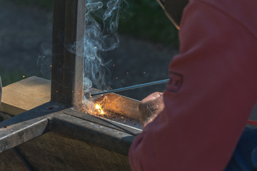 A man welds a metal product with arc welding machine, lots of smoke, bright lights and sparks