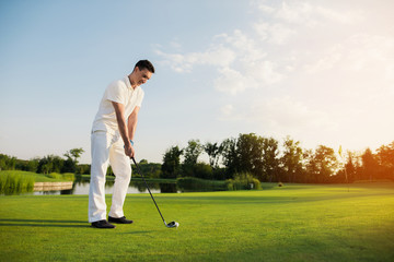 A man in a white suit plays golf. He is preparing for another ball hit