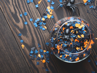 Halloween orange and black confetti with spiders and spider net on dark rustic wooden background. Holiday decoration symbols
