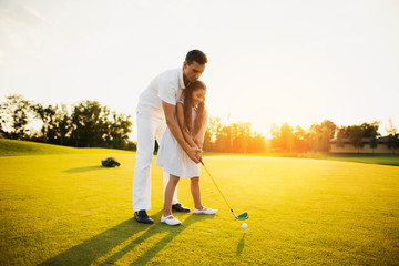 A man is teaching a girl who is preparing to make her first hitting with a golf club