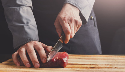 Chef cutting filet mignon on wooden board at restaurant kitchen
