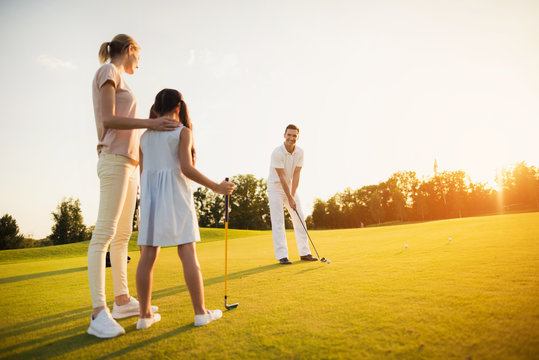 Family playing golf at sunset. A woman and a girl are looking at a man who is preparing to make a hit