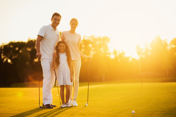 Family posing on a golf course holding a golf club on a sunset background