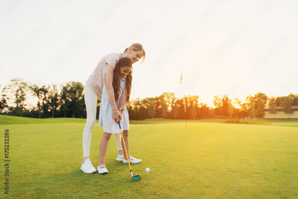 Wall mural a woman is teaching a girl to play golf. the girl is preparing to hit, the woman is standing behind 