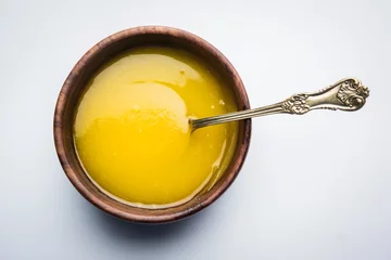 Fototapeten Ghee or clarified butter close up in wooden bowl and silver spoon, selective focus   © StockImageFactory