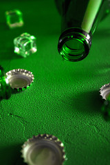 Conceptual beer background. Green beer bottles with ice cubes and lids on a green background