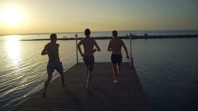 Group of friends running and jumping off sea pier in the water rapid slow motion