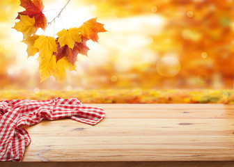 Empty wooden deck table with tablecloth over bokeh autumn leaves background. Kitchen background, product montage display. Mock up .