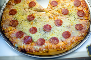 Pizza with salami and cheese is on the shop window in the store