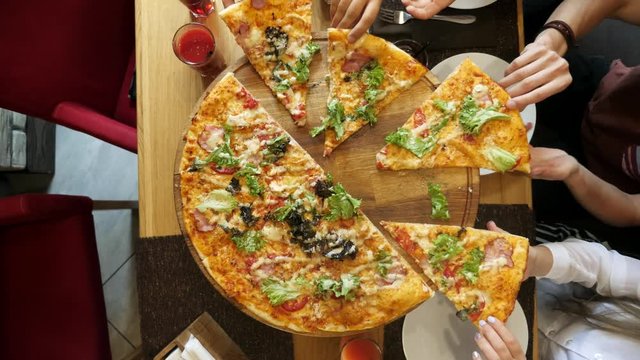 Hands taking pizza cuts from plate on table.