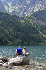 Young couple sitting on the rock at Morskie Oko Lake, tatra National Park, Zakopane, Poland