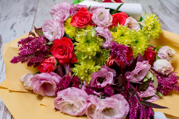 A beautiful bouquet of pink eustoms, a yellow chrysanthemum, a red and pink rose, on shabby white wooden background