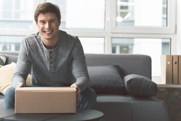 Beaming young male keeping cardboard box