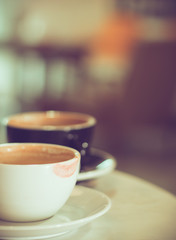 two cups of hot coffee at cafe, white one with red lipstick mark, black one with beautiful bokeh as background, selective focus, vintage tone