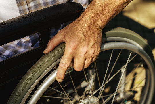 Close up. The old man holds his hand to the wheel of a wheelchair