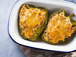 Bell peppers stuffed with mixed cereals, meat and cheese baked in enamel tin on blue