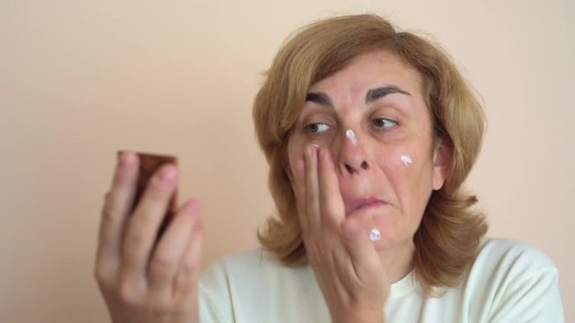 Middle aged woman applying cream on her face    