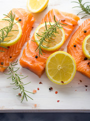 Raw salmon pieces on wooden board with herbs, salt and spices