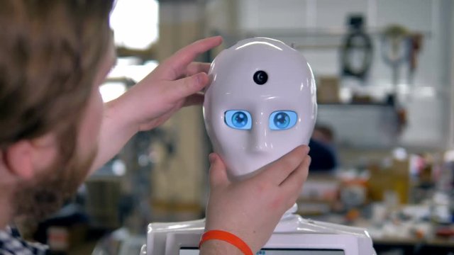 An engineer puts a white mask on robots face. 