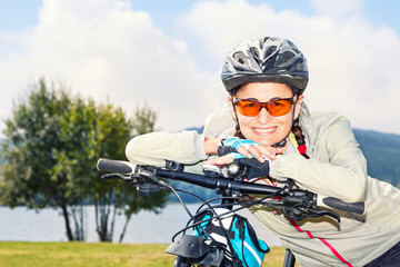 Portrait of mature female tourist cyclist posing on background of mountains and lake, looking at camera and smiling.