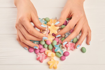 Obraz na płótnie Canvas Female hands and colorful candies. Woman manicured hands and multicolored tasty candies on white wooden background close up.